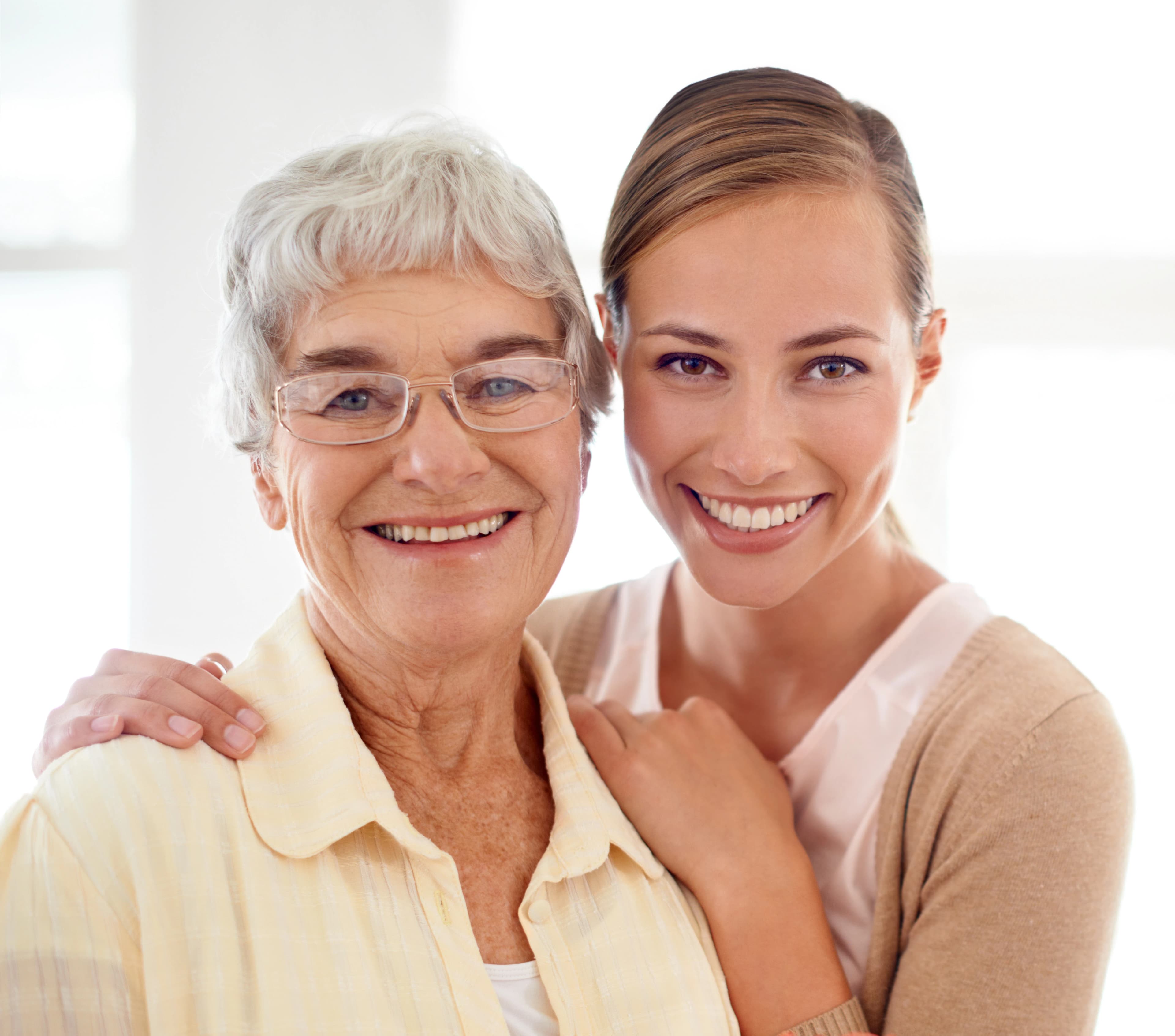 A family member shares a warm, unhurried moment at home with their elderly loved one in soft window light.